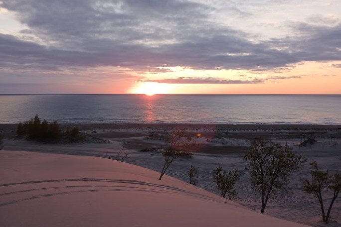 Sunset over a beach with distant trees and a cloudy sky.