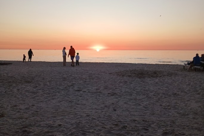 Silhouettes of people on a beach at sunset with colorful sky.