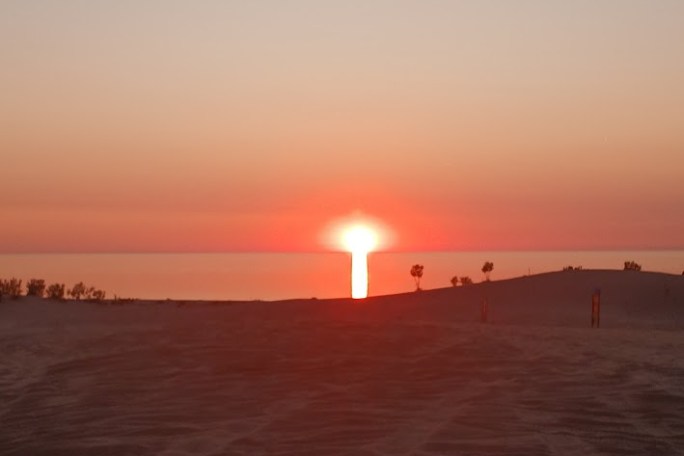 Sunset over sand dunes with a clear sky and distant horizon.